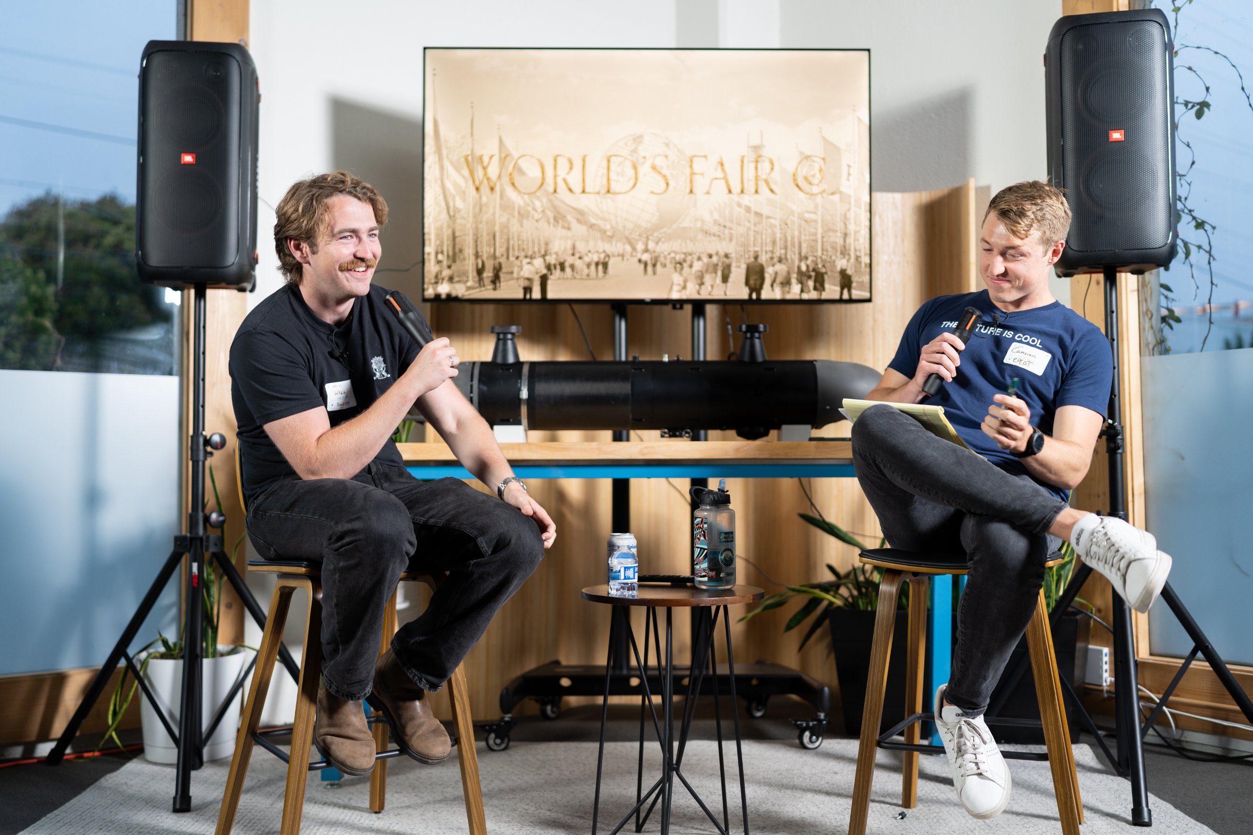 Will O’Brien of Ulysses laughing on stage with Cam Wiese at a Pioneers talk, with Ulysses’ underwater robot behind them